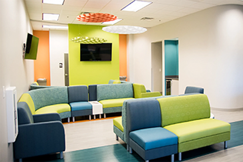 Modern waiting room with colorful seating, TVs, and bright walls.