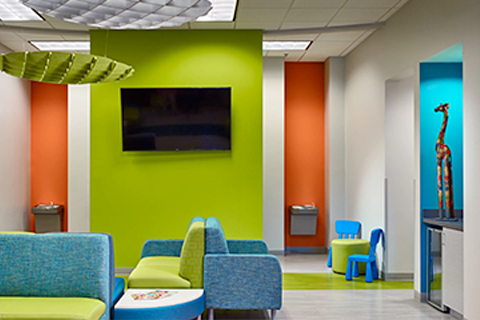 Waiting room with lime green, teal, and orange accents, blue and green seating, and a mounted TV.