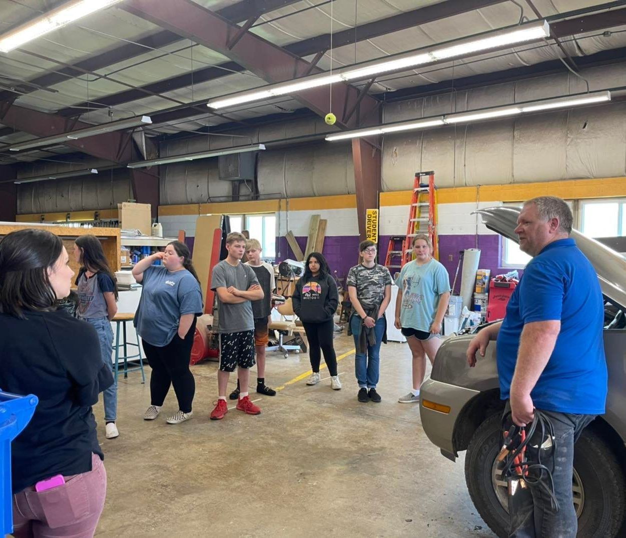 A group of people are standing around a car in a garage.