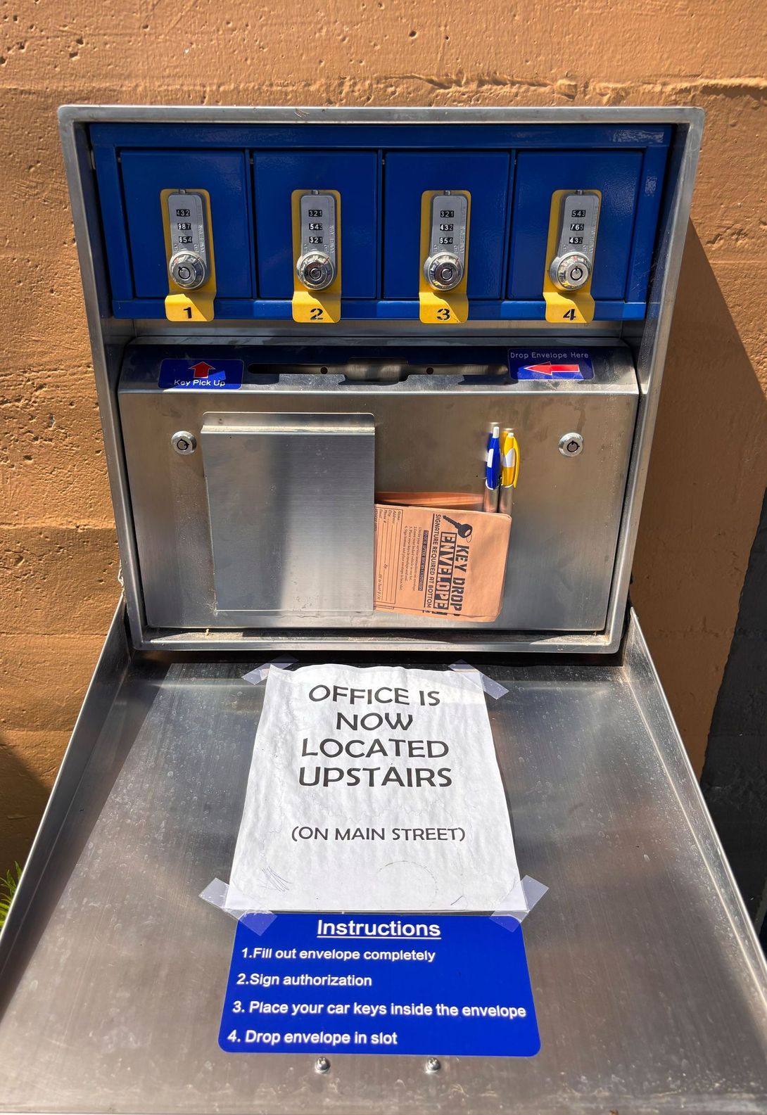 A metal box with a sign on it that says office is now located upstairs
