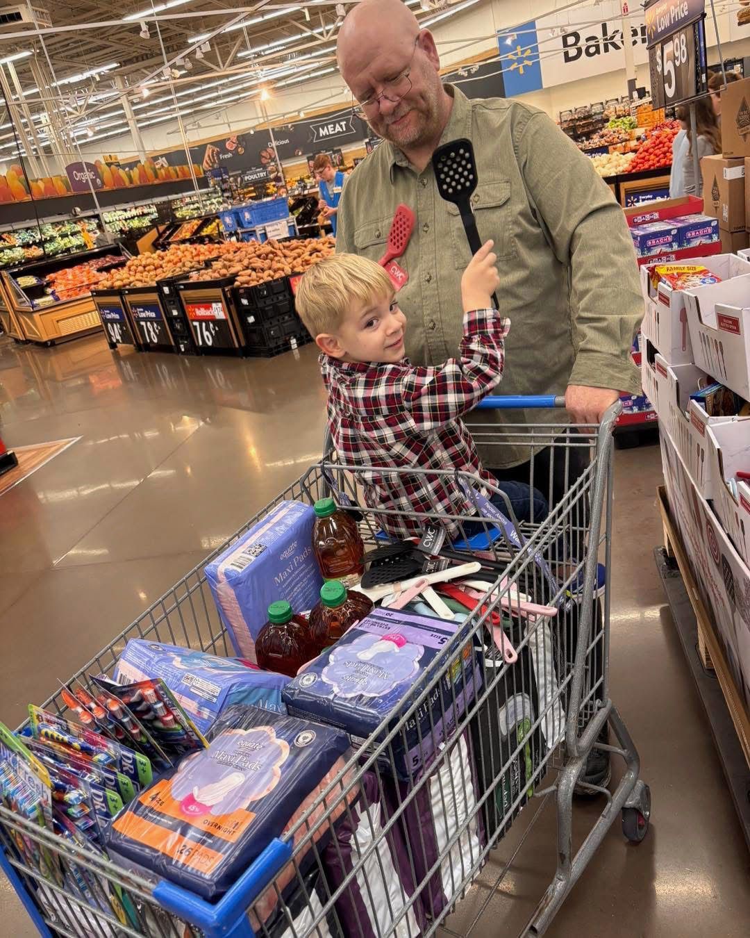 DJ Keilholz is pushing a shopping cart with a child in it in a grocery store.