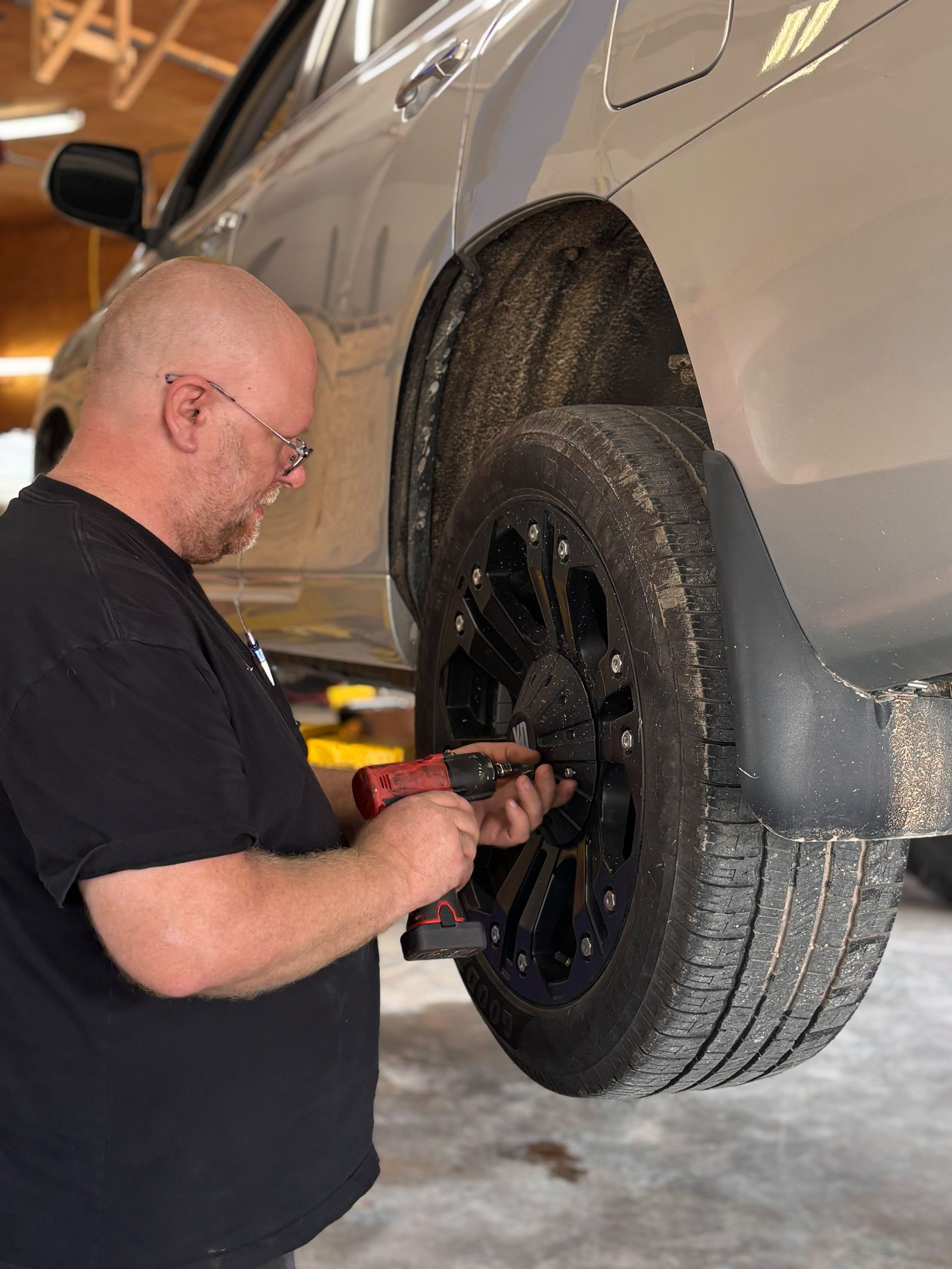 A man is working on a car wheel with a drill.