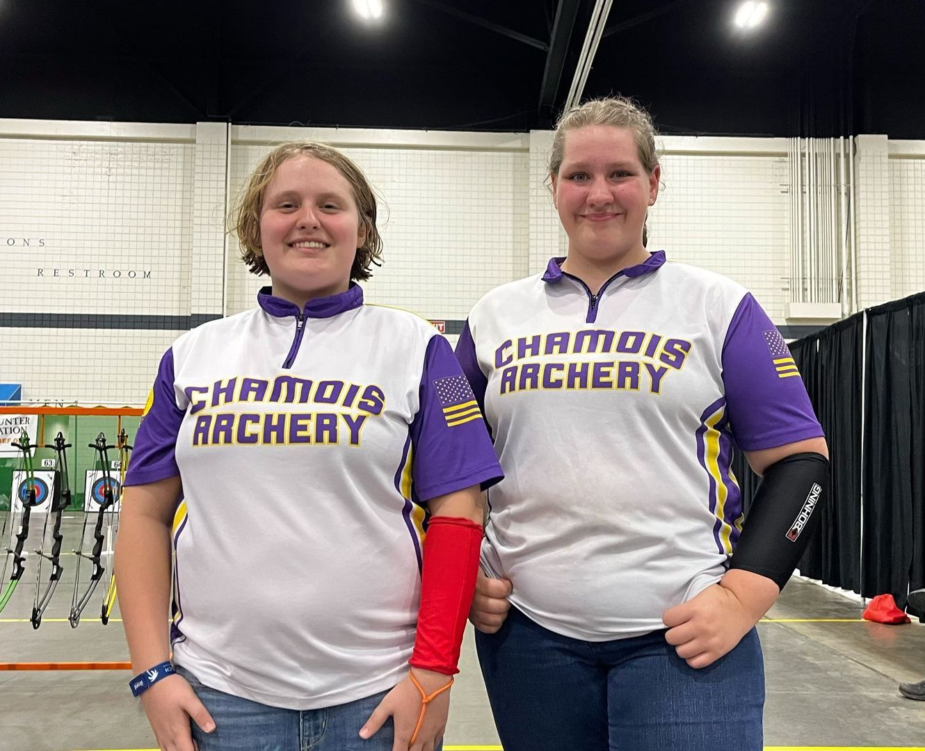 Two women wearing chamois archery shirts are standing next to each other.
