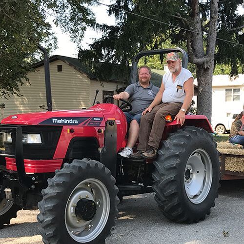 DJ Keilholz and his dad are sitting on top of a red tractor.
