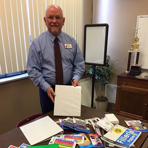A man in a suit and tie is standing in front of a desk holding a piece of paper.