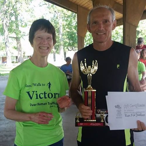 A man holding a trophy next to a woman wearing a green shirt that says victory