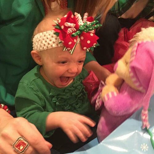 A baby wearing a headband and a ring is playing with a stuffed animal