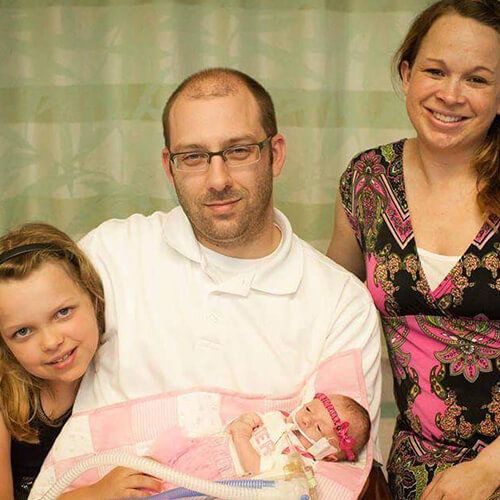 A family is posing for a picture with a newborn baby.