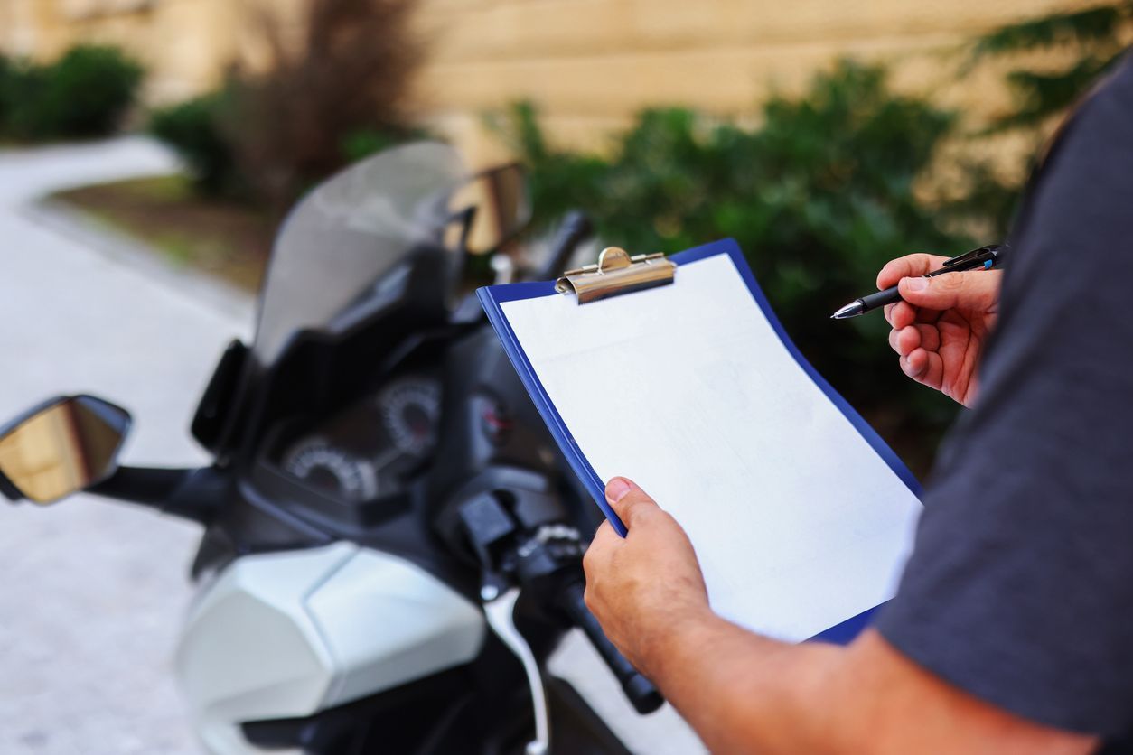 A man is writing on a clipboard in front of a motorcycle.