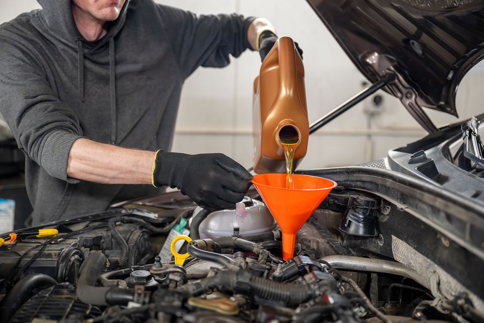 A man is pouring oil into a car engine through an orange funnel.