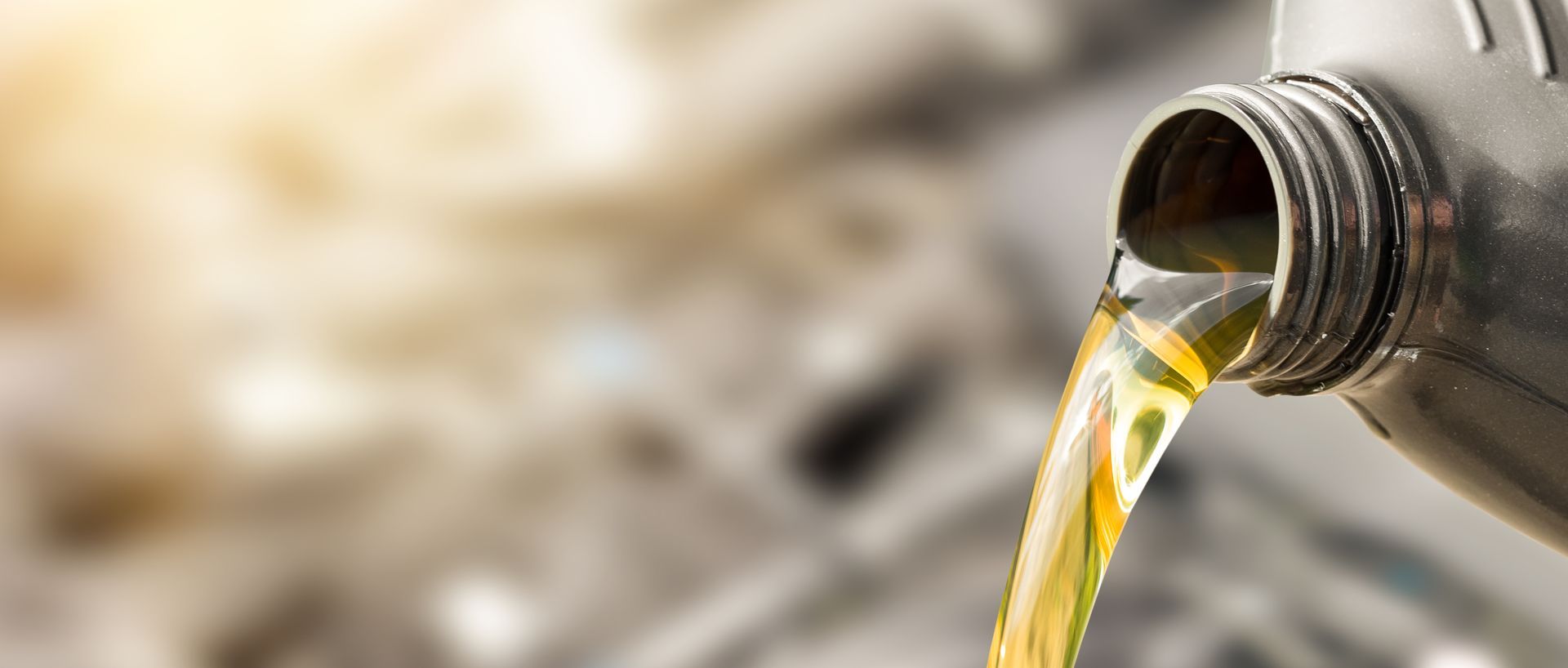 A close up of a bottle of oil being poured into a car engine.