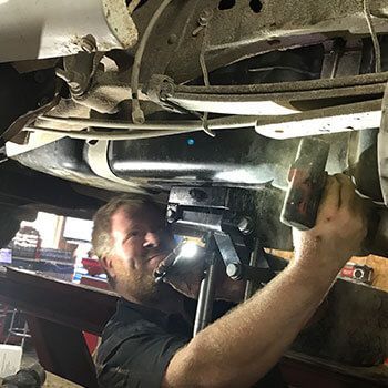 A man is working under a car with a flashlight.