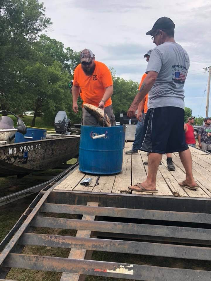 A group of men are standing on a dock holding a fish in a blue barrel.