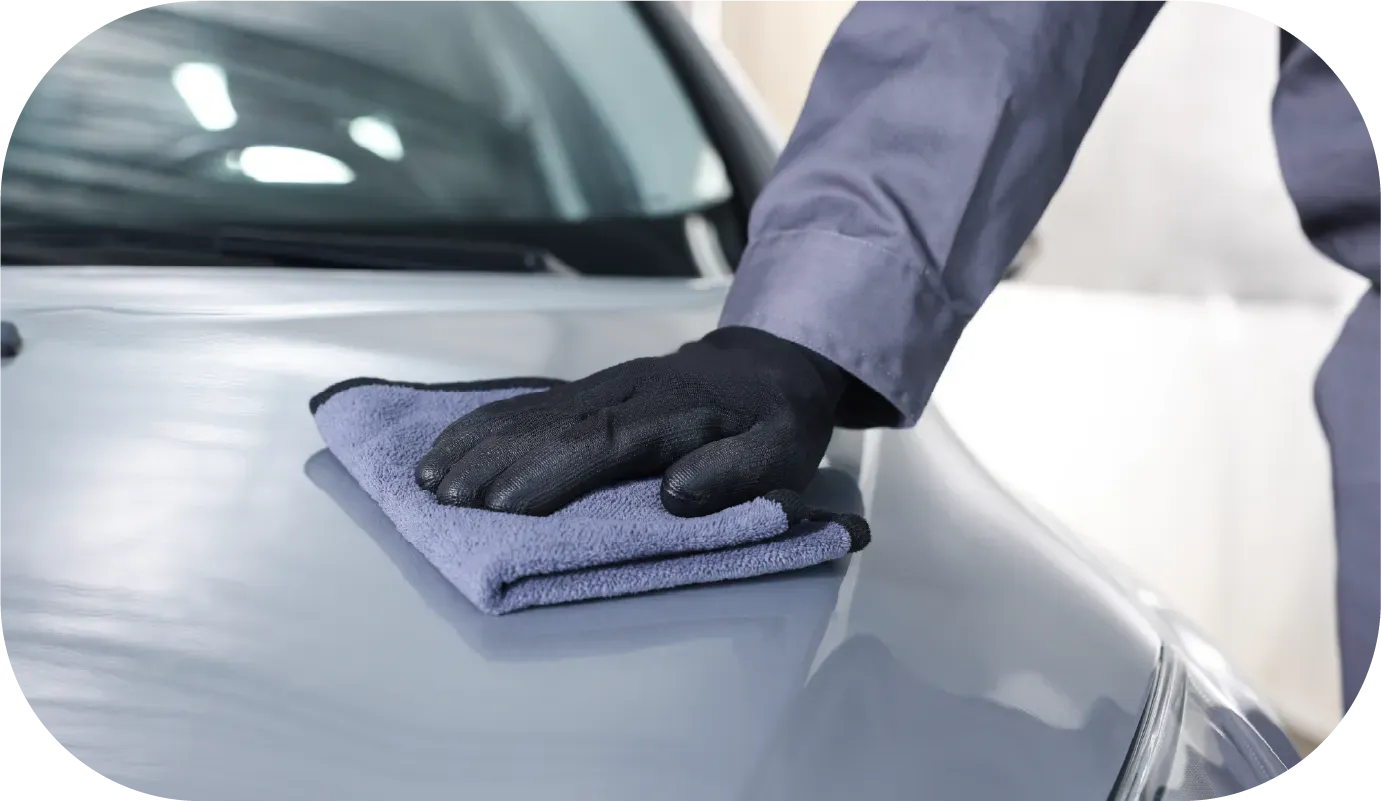 Black McLaren sports car parked next to a van and a metal fence; sunny outdoor setting.