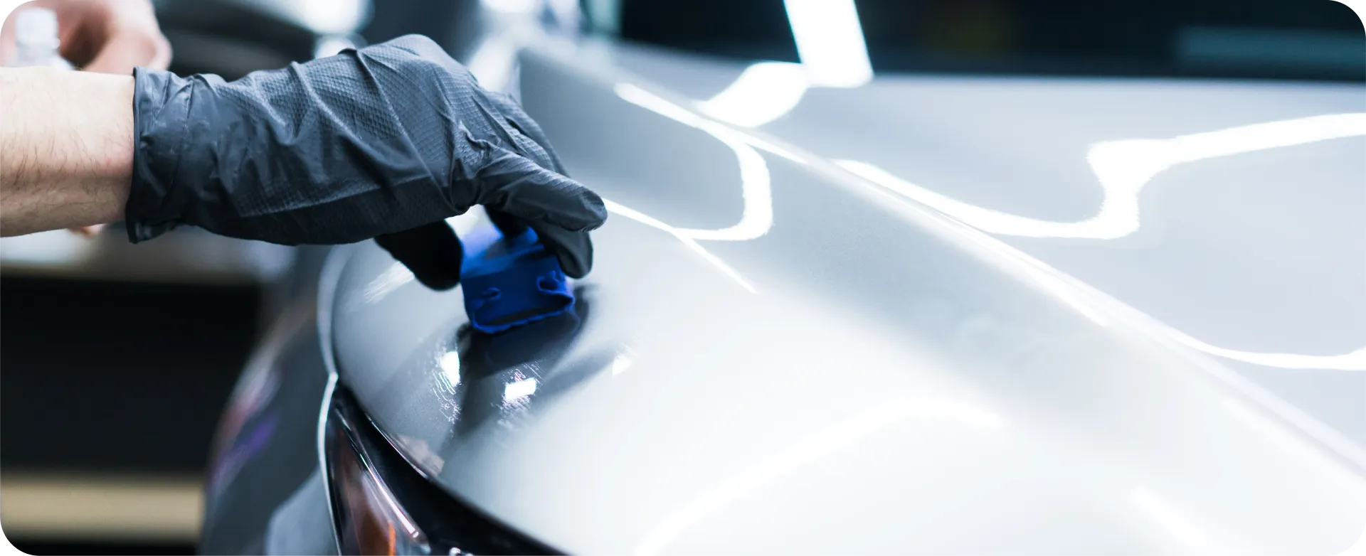 Gloved hand applying a blue coating to a blue car panel.