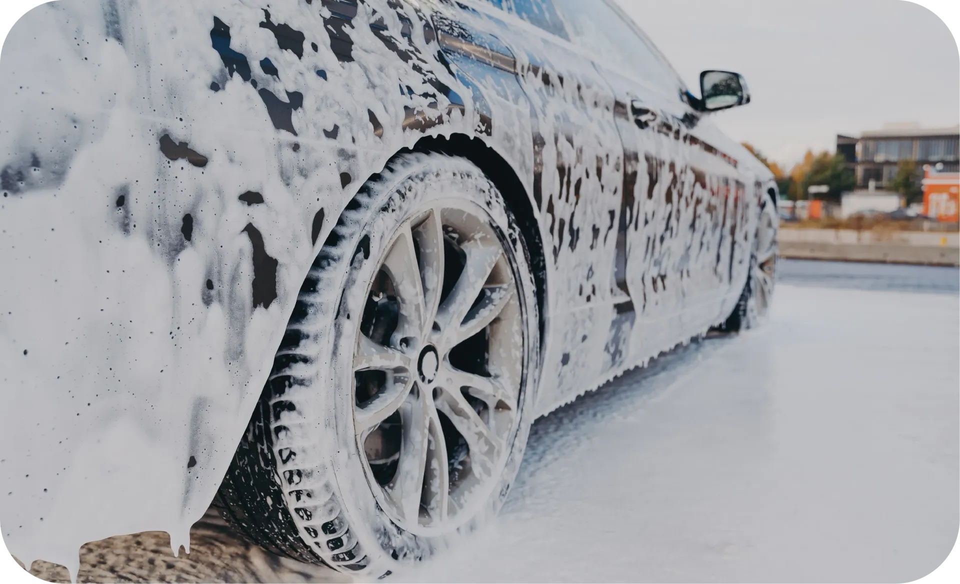 Silver sports car covered in white foam, parked outdoors for cleaning.