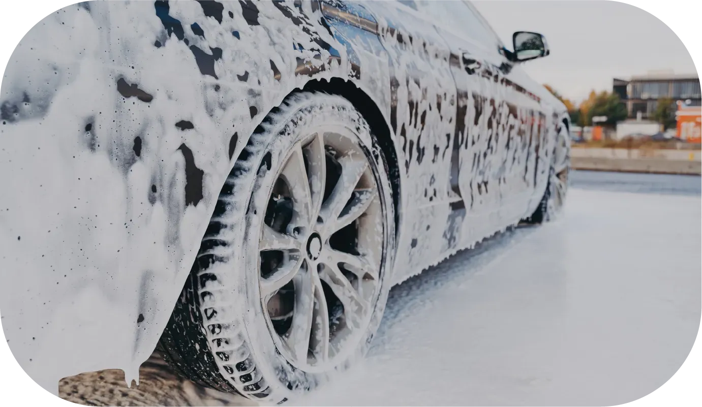 Silver sports car covered in white foam, being washed outdoors.