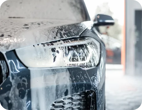 Gray McLaren sports car with doors open, on gravel, trees in background.