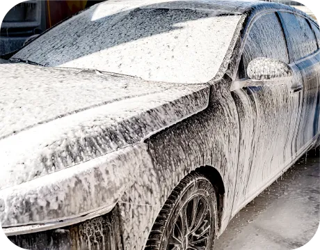 Silver car covered in foamy car wash soap, parked on a brick driveway in front of a house.