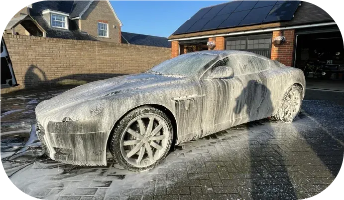 Silver sports car covered in white foam being washed outside a house.