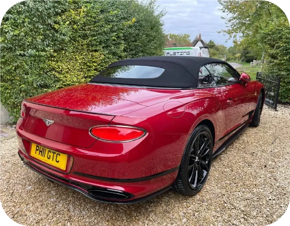 Red Bentley convertible parked on gravel. Black top and wheels.