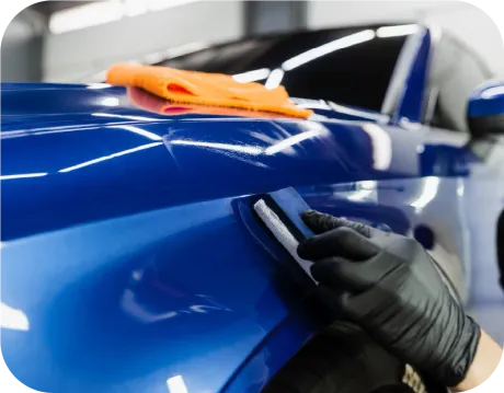 A gloved hand applies ceramic coating to a blue car with a microfiber cloth on the hood.