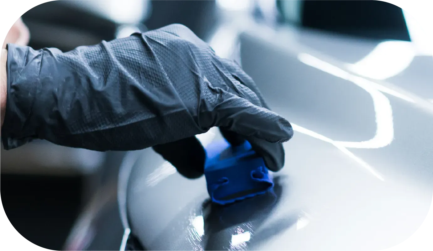 Person in black gloves applying coating to a blue car with orange cloth on top.
