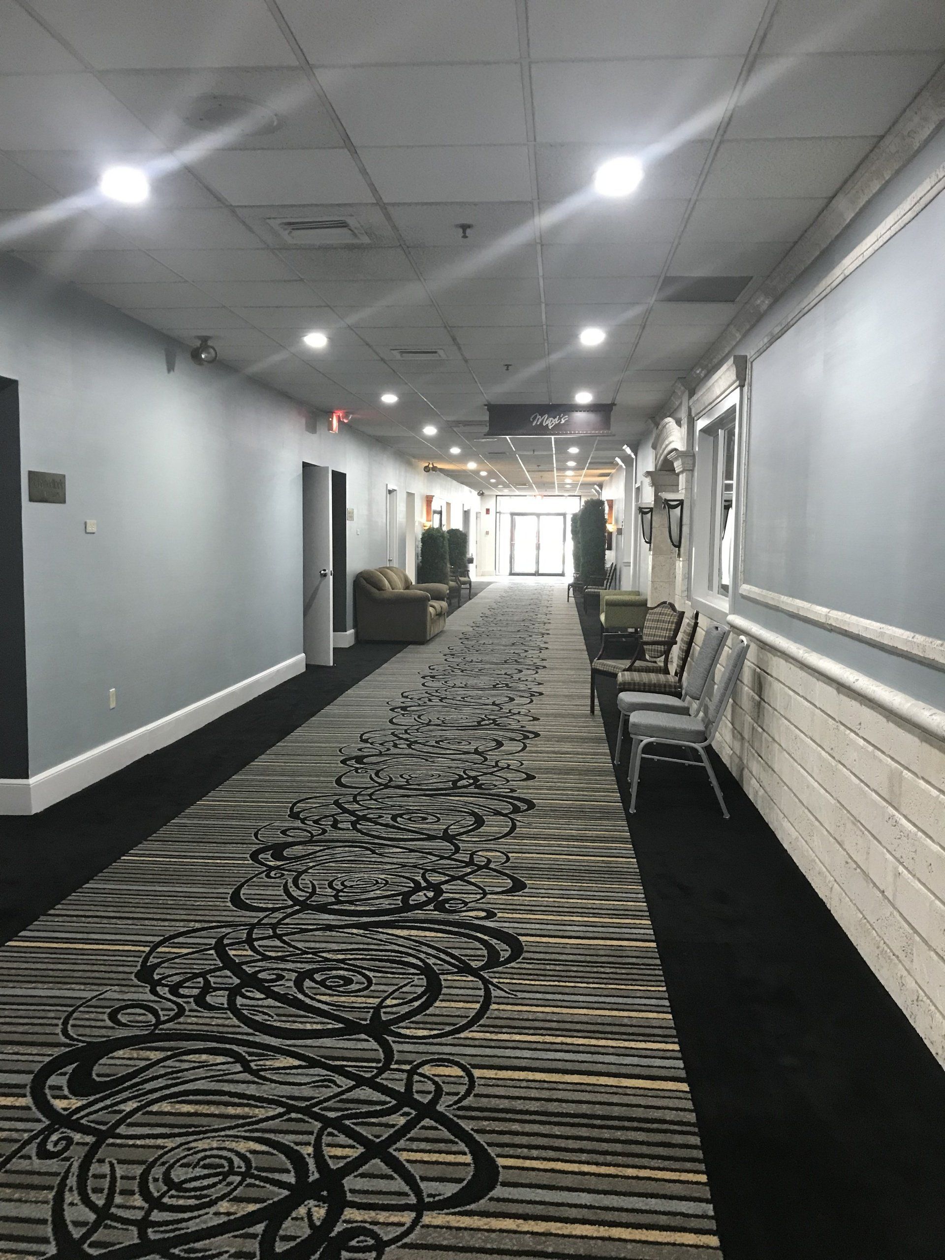 A long hallway with a carpet and chairs in a hotel.