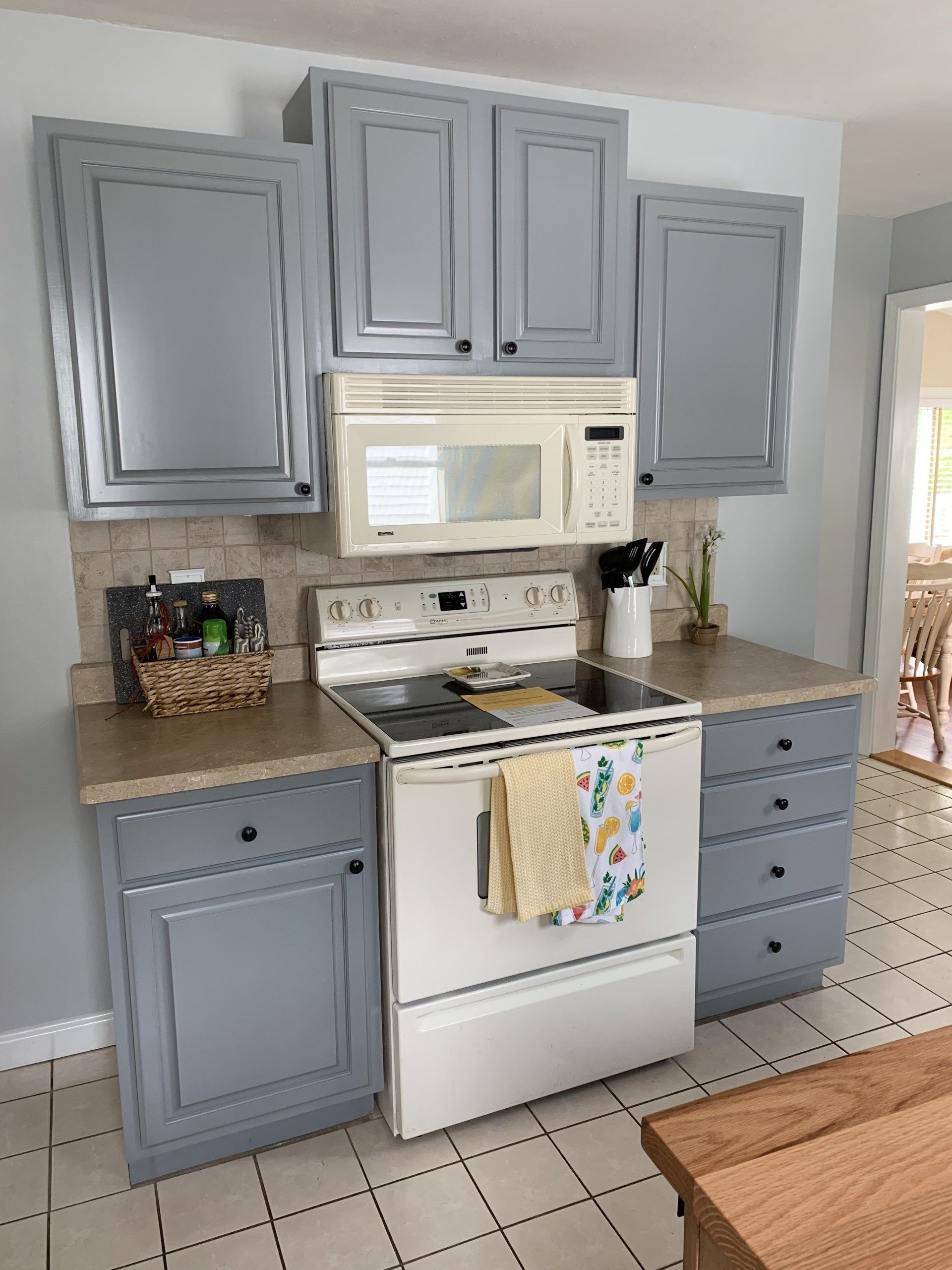 A kitchen with gray cabinets , a white stove , a microwave , and a sink.