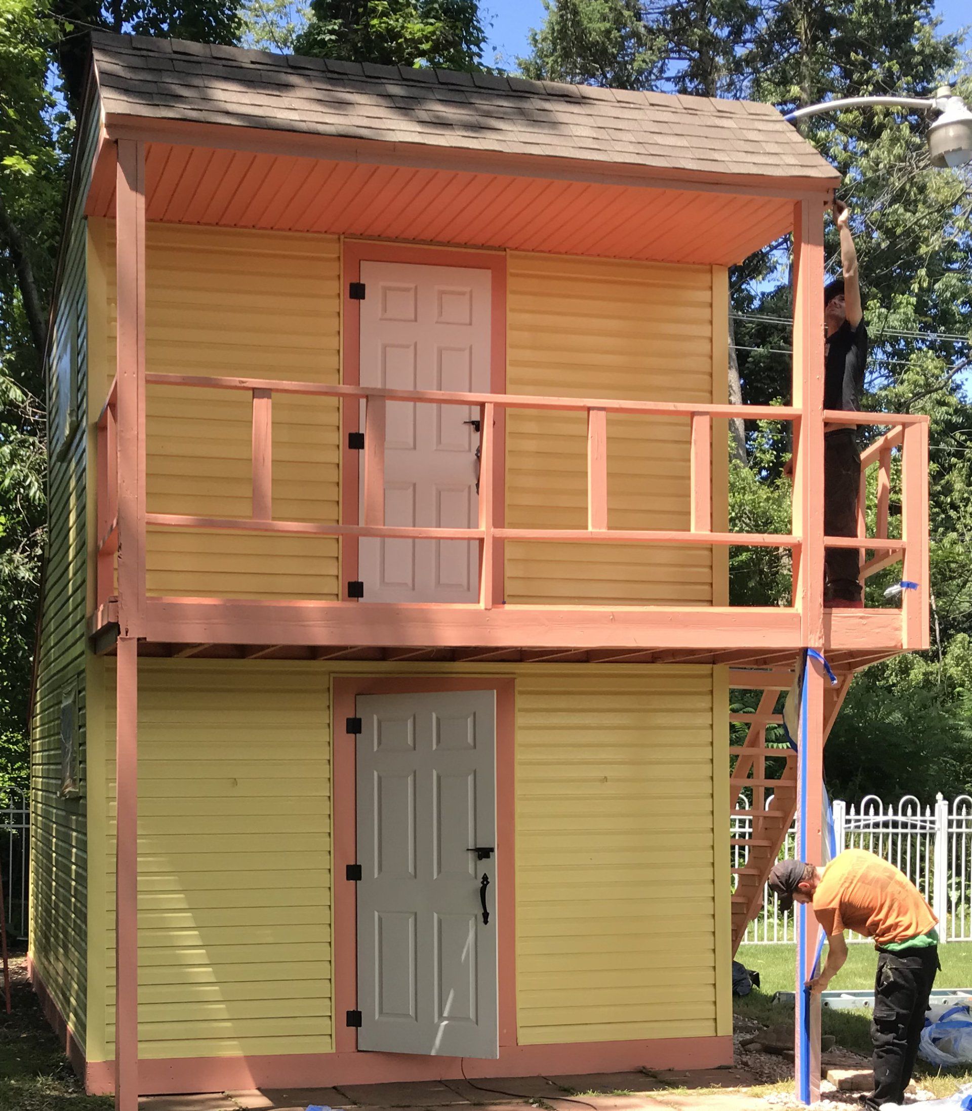 Two men are working on a yellow house with a balcony
