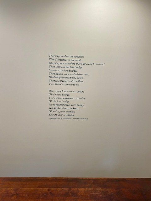 A white wall with a poem on it and a wooden floor.