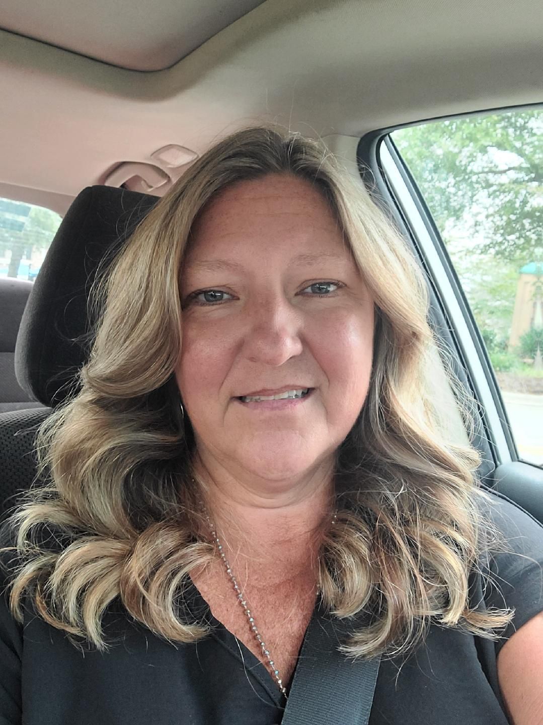 A woman is sitting in a car wearing a seat belt and smiling.