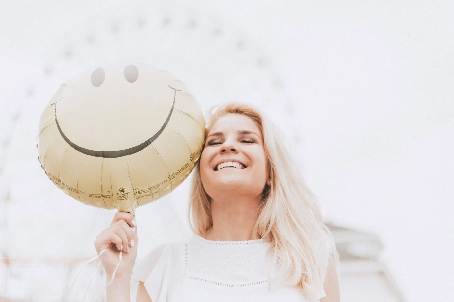 A woman is holding a smiley face balloon in front of her face.