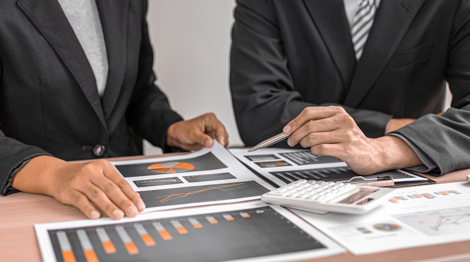 Two businesspeople in suits reviewing printed charts and graphs at a meeting table