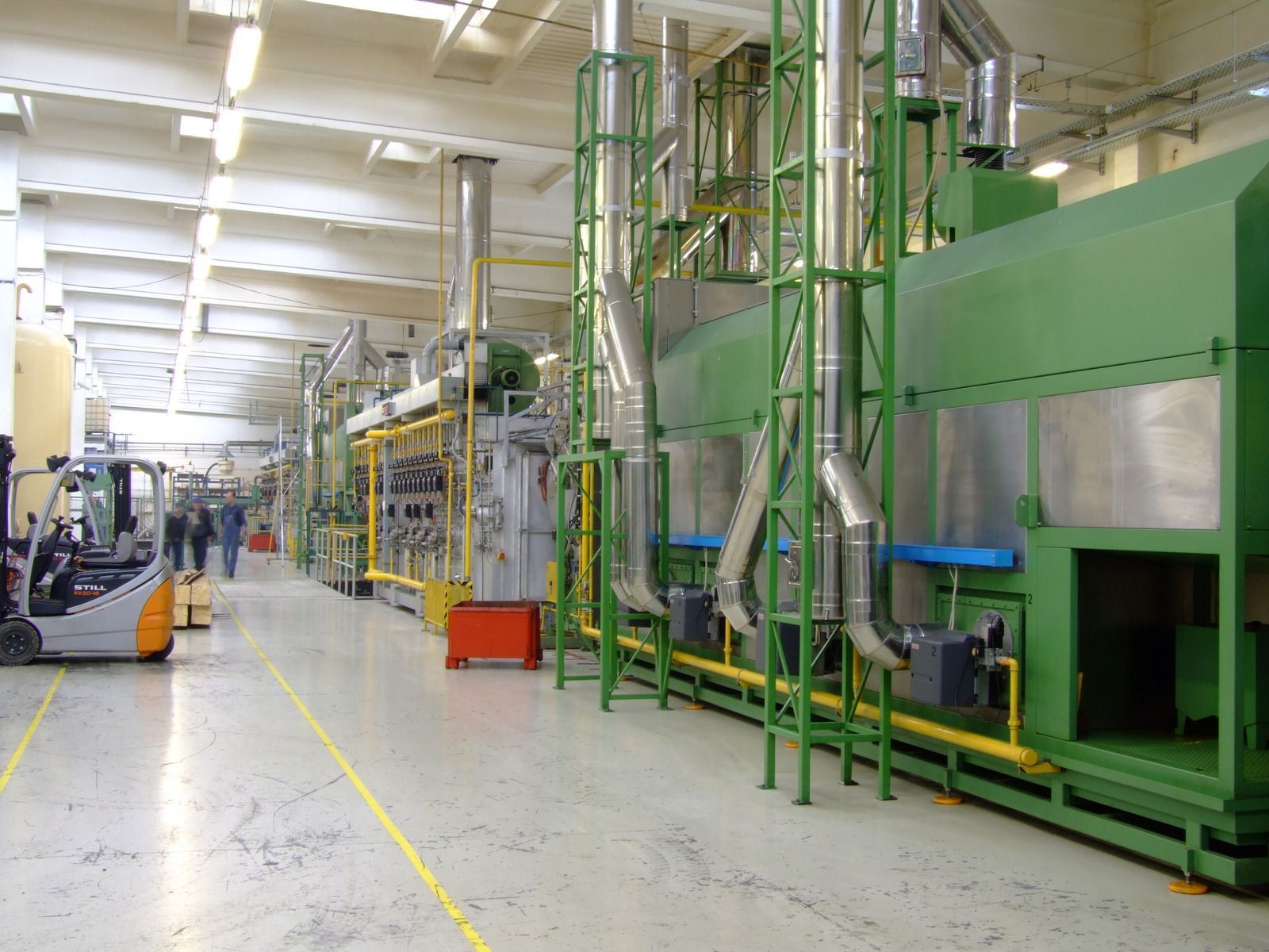 Industrial factory interior with large green machinery, metal framework, and a wide aisle under bright ceiling lights