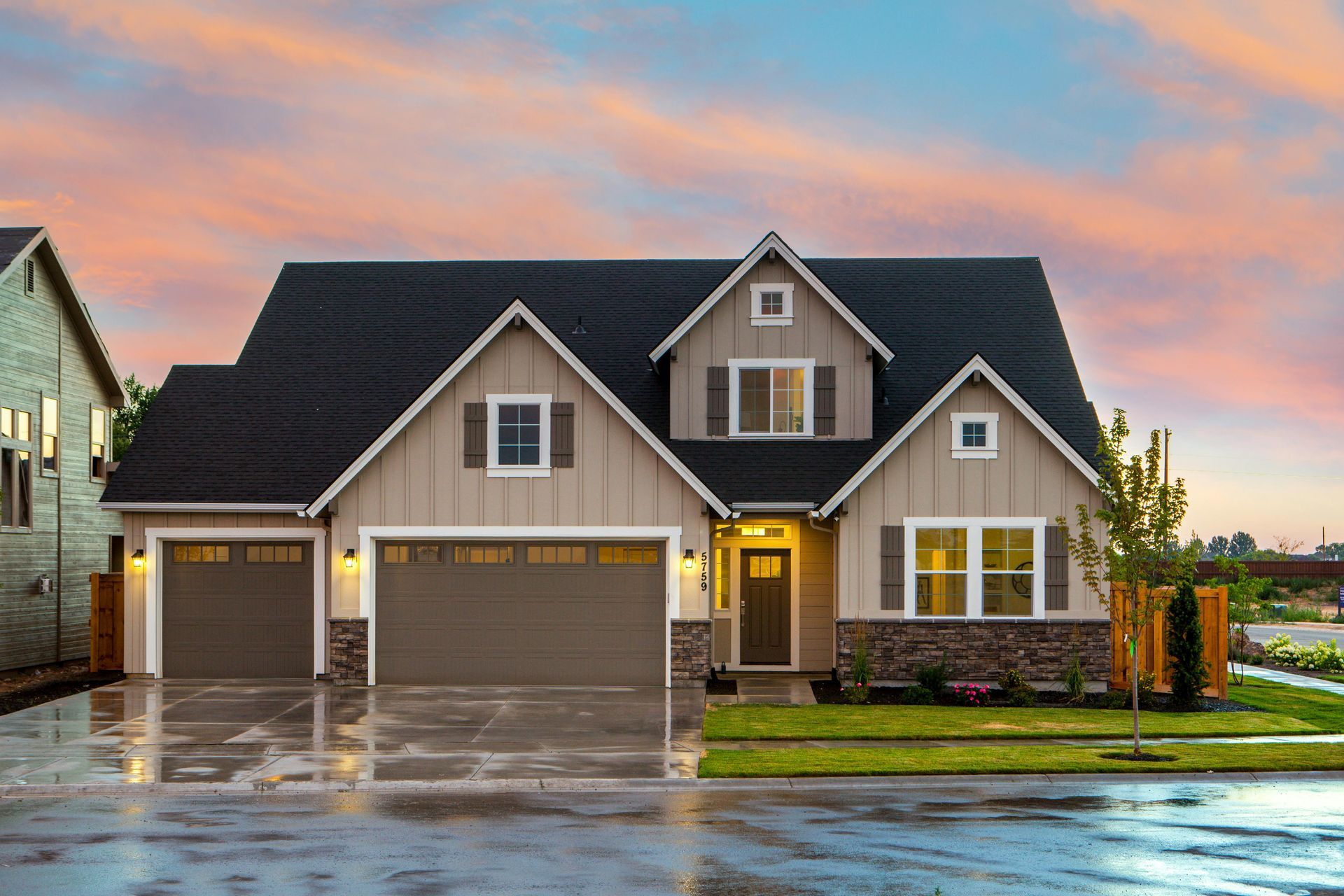Suburban house with three-car garage at sunset, warm lights glowing on a wet driveway