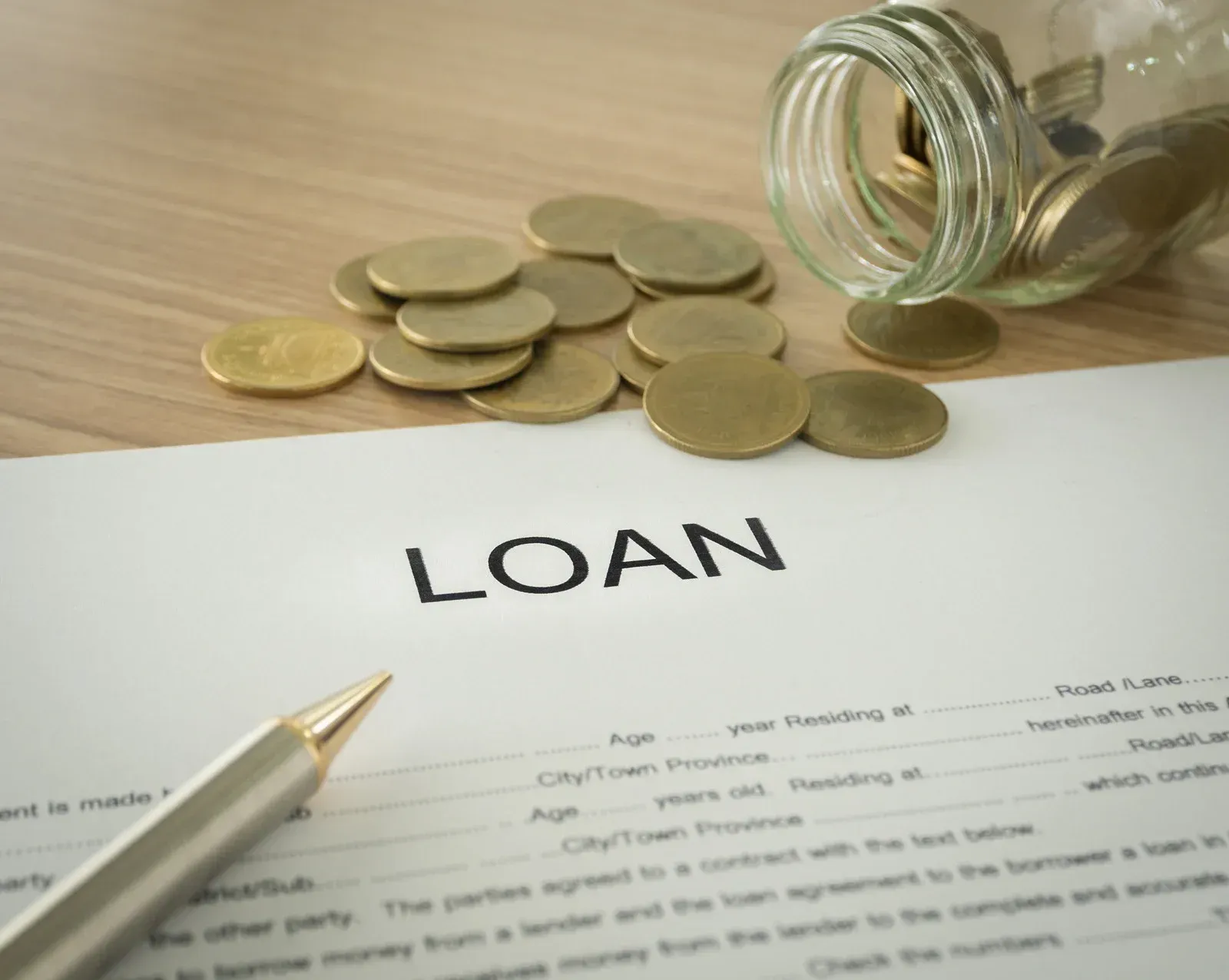 Loan document with pen, coins, and an open jar on a wooden table