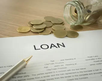 Loan document with pen and spilled coins on a wooden desk