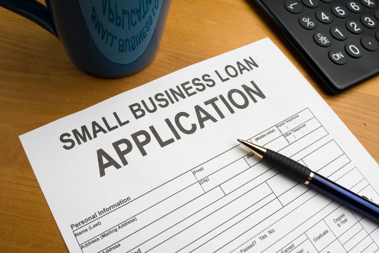 Small business loan application form on a desk with pen, calculator, and coffee mug