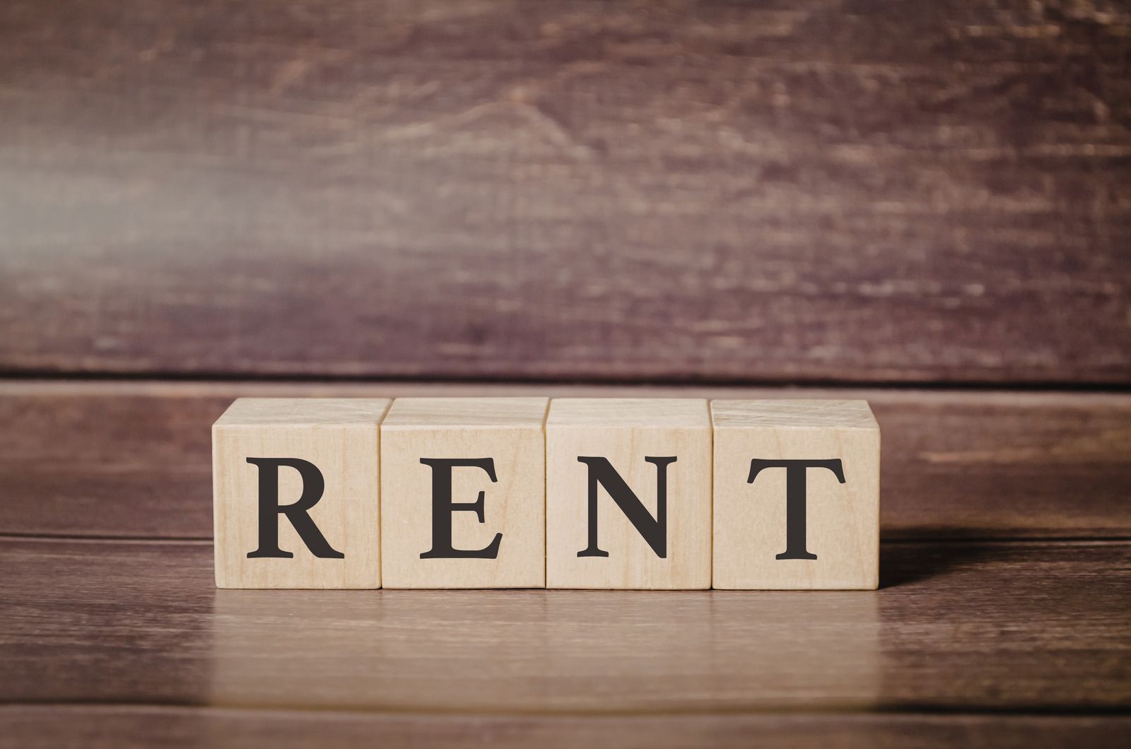 Wooden blocks spelling “RENT” on a rustic wood surface