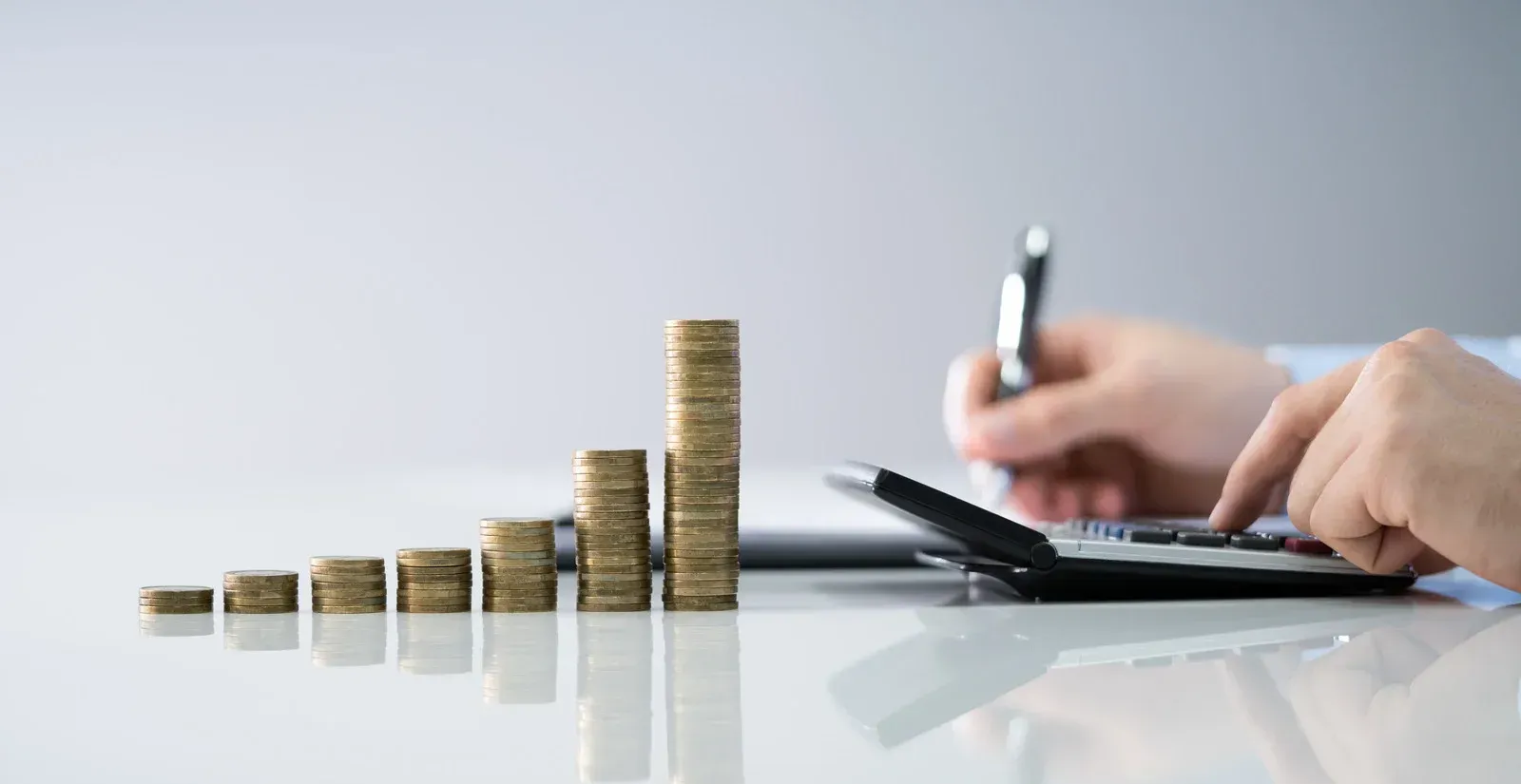Coins stacked beside hands writing on a calculator at a desk