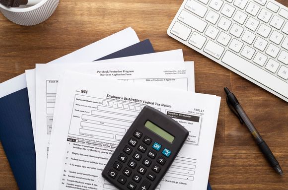 Calculator on financial papers with pen and keyboard on a wooden desk