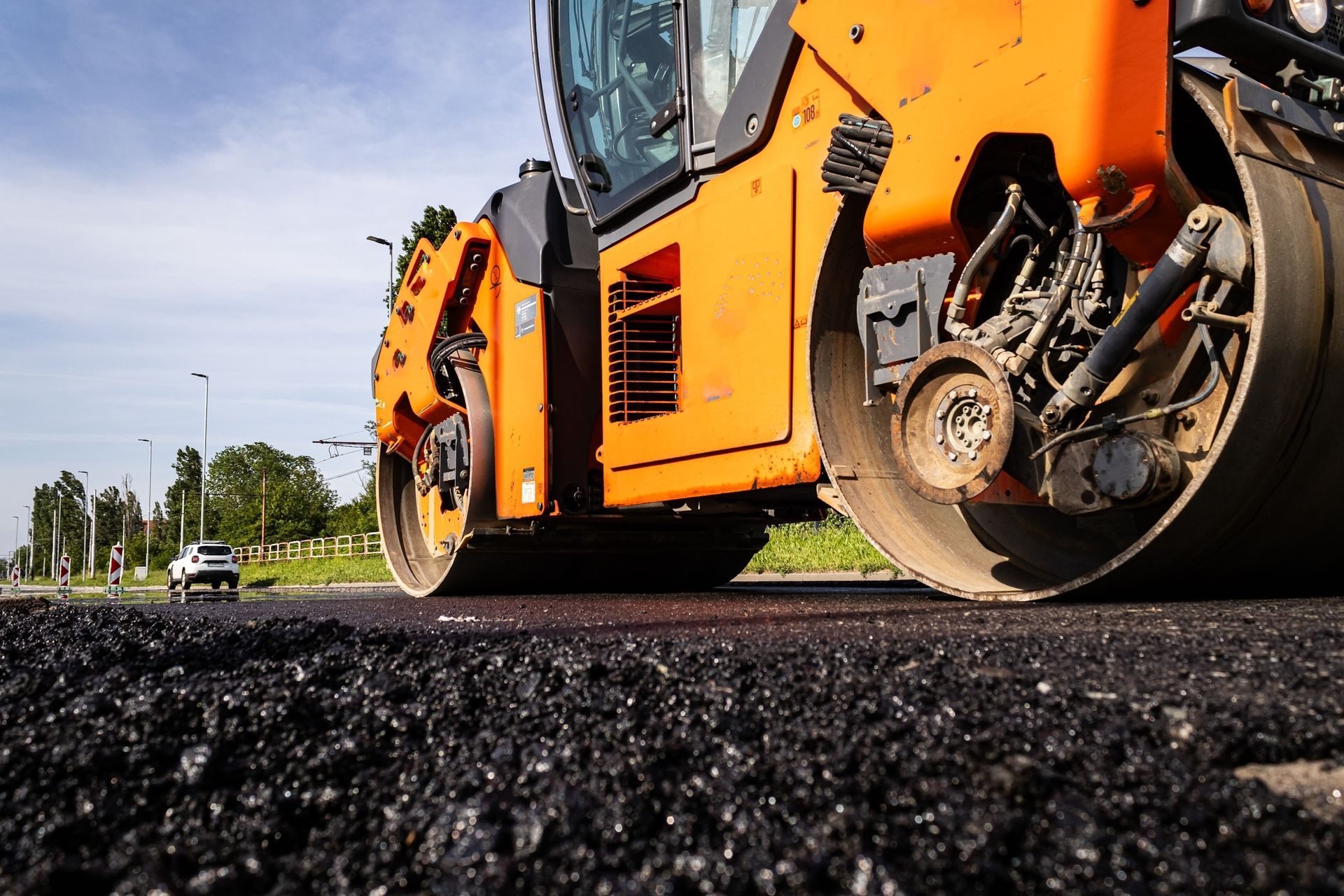 A large orange roller is rolling asphalt on a road.