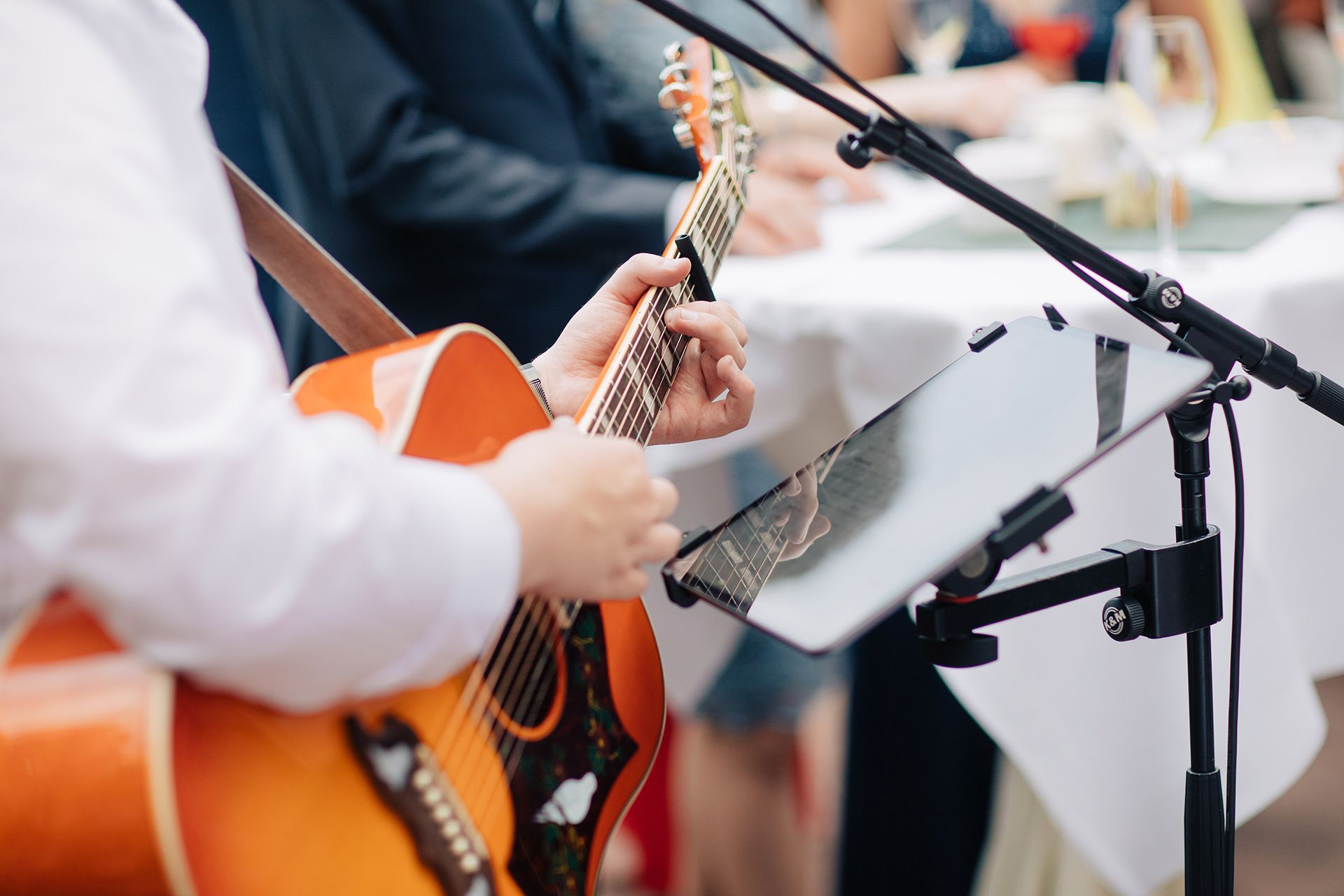 Orange guitar being played beside a microphone stand and sheet music during a performance