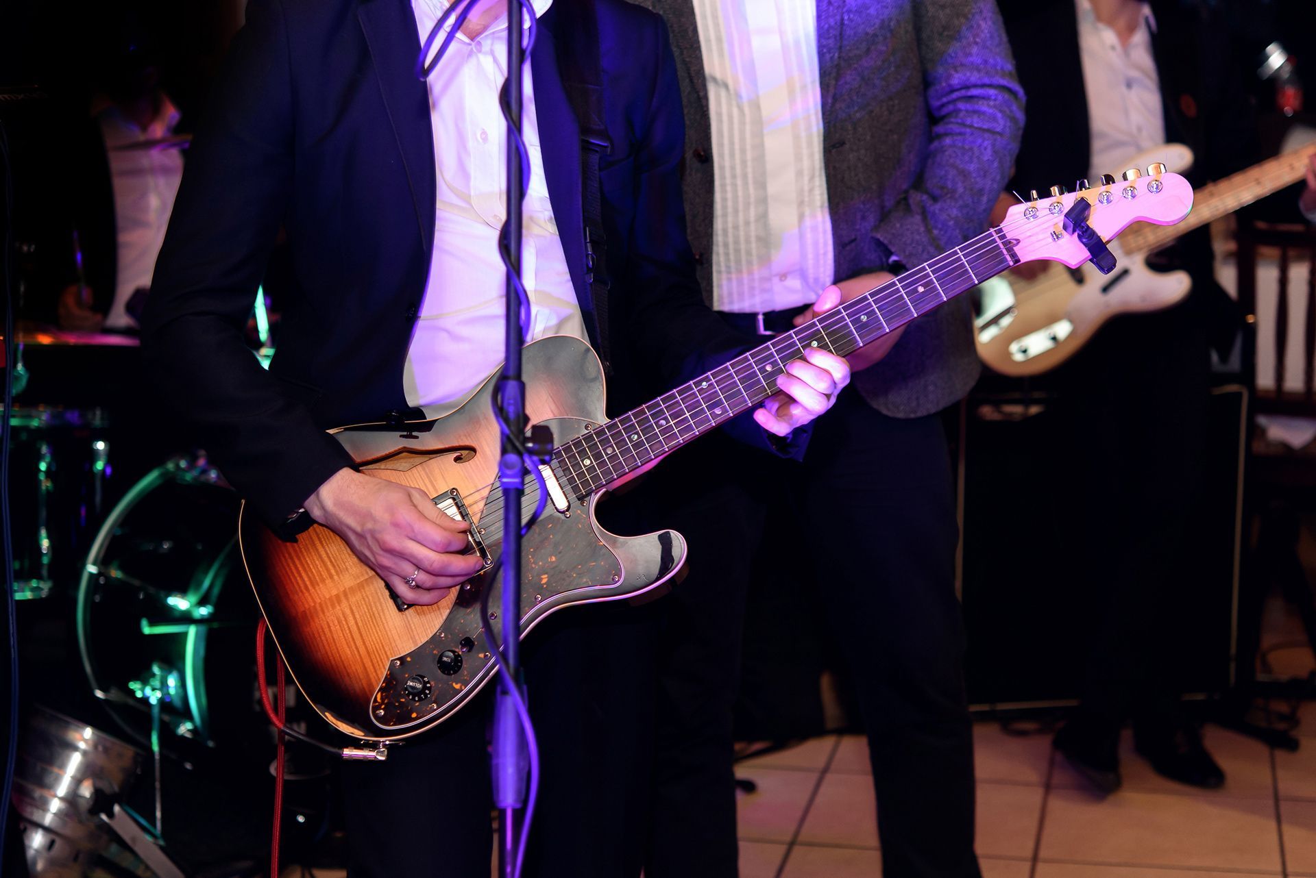 Musician playing a sunburst electric guitar onstage under purple lighting
