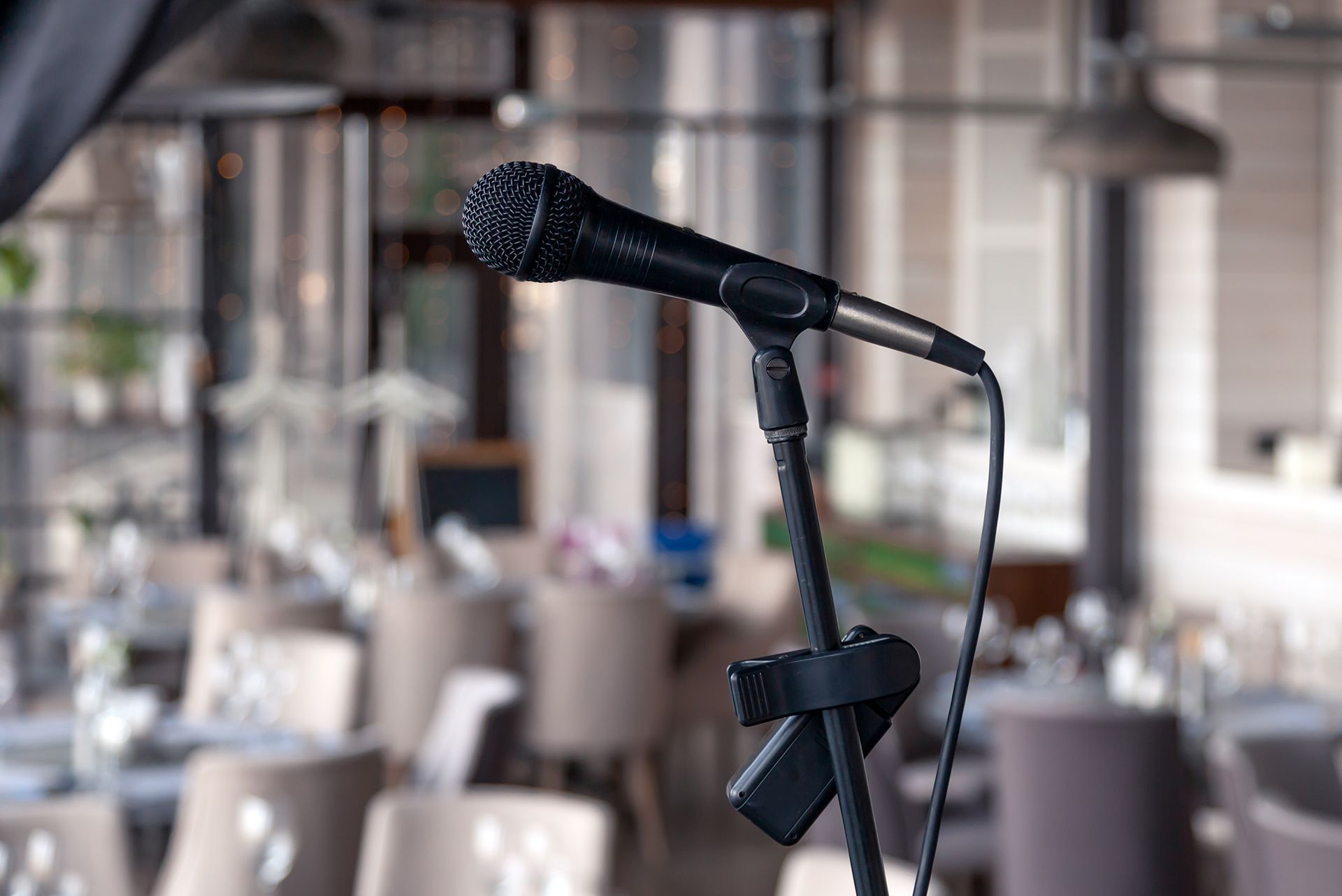 Black microphone on a stand in a blurred restaurant or event venue setting