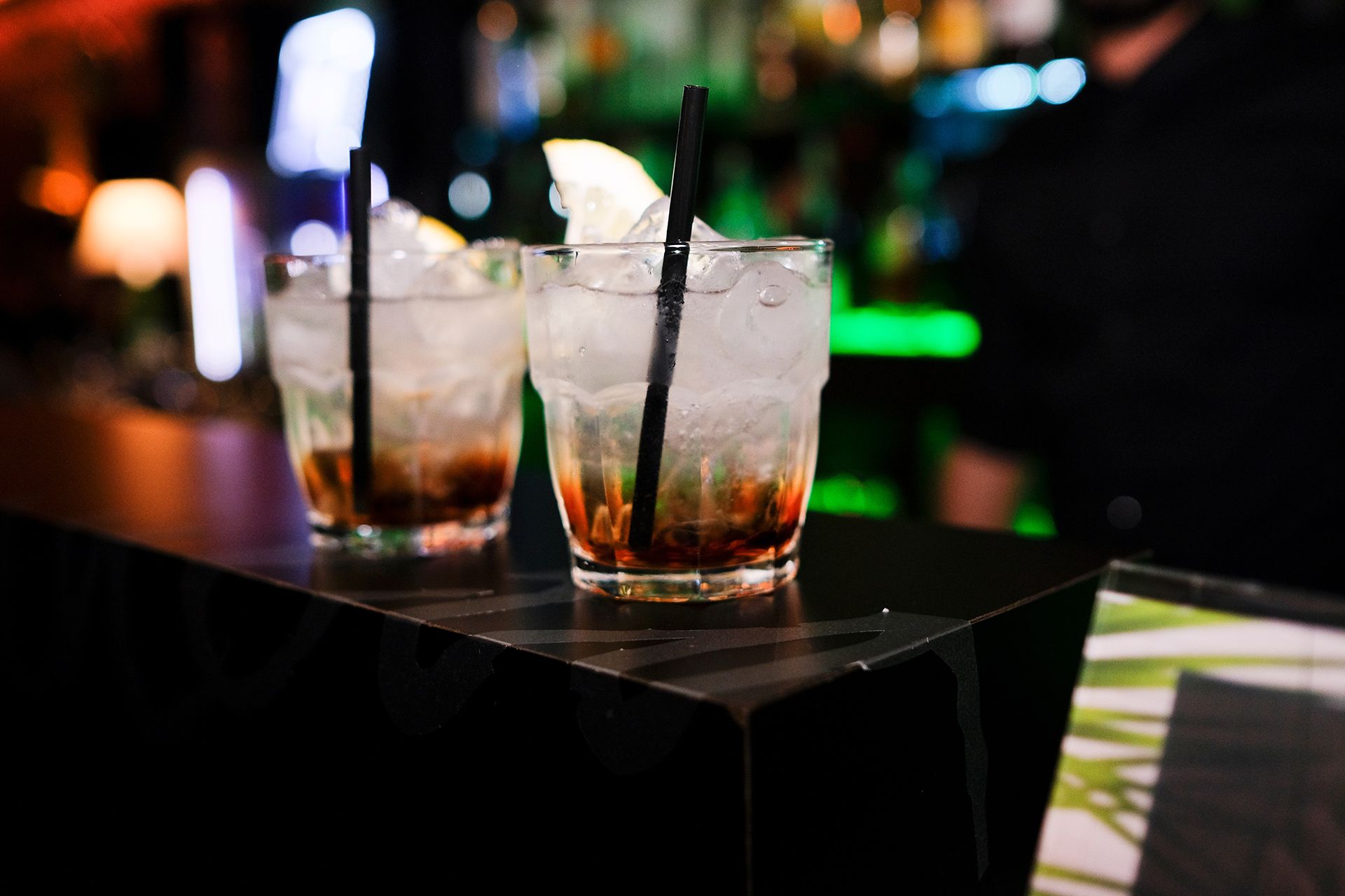 Three cocktail drinks with straws on a bar counter in a dimly lit lounge.