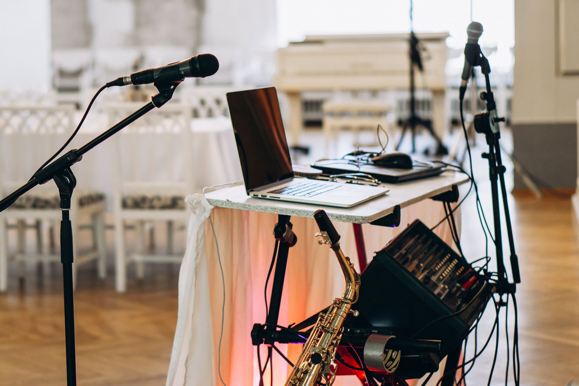 Microphones and a laptop on a table with audio equipment and a saxophone in a bright room.