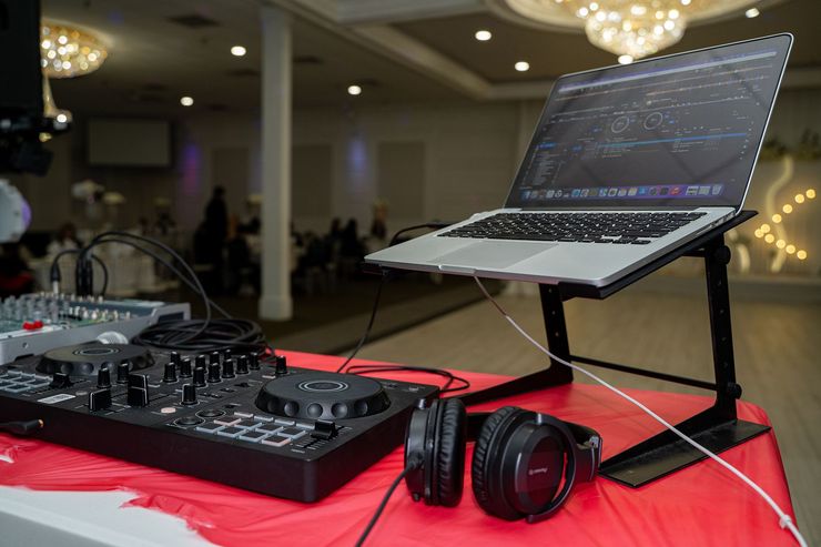 DJ setup with laptop on stand, mixer, and headphones on a red table in a banquet hall