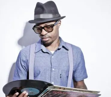 Man in a black hat and glasses looking at a vinyl record in bright light